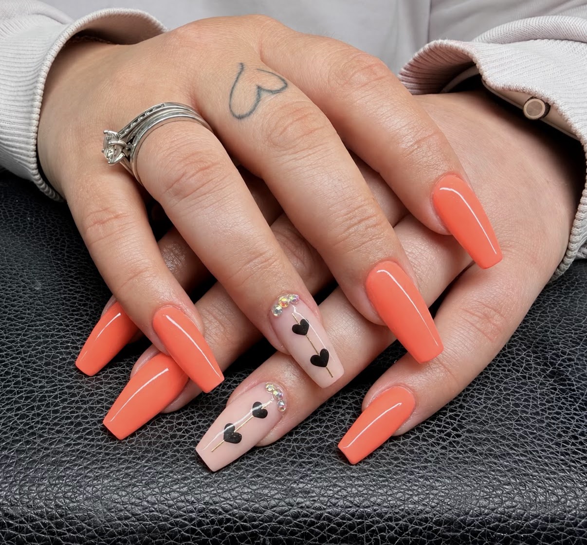 Oranje coffin acrylnagels, twee nude nagels met zwarte hartjes en steentjes